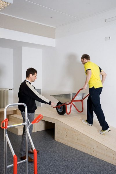 Patient schiebt Schubkarren eine Rampe hoch unter Anleitung eines Therapeuten im Rahmen der medizinisch beruflich orientierten Rehabilitation des VAMED Rehazentrums Karlsruhe 