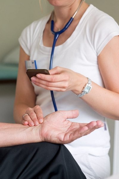 Nahaufnahme einer Aerztin die einem Patienten den Blutdruck misst, nur Oberkoerper und Arme sind zu sehen