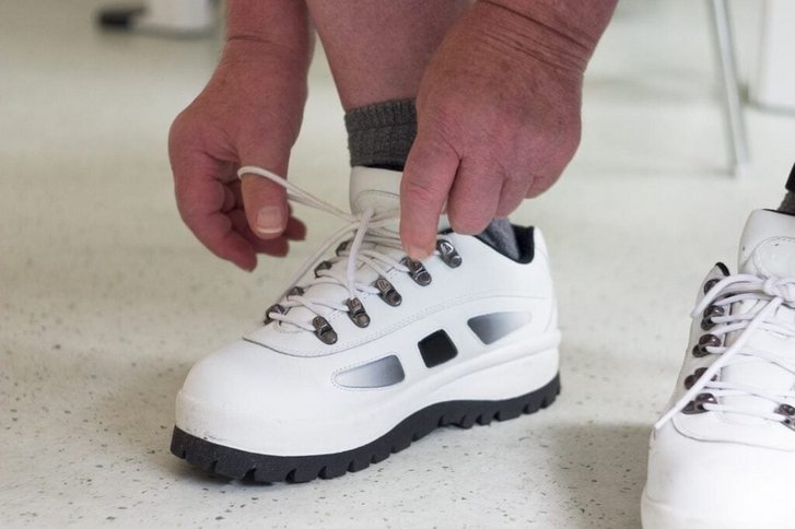 Nahaufnahme von Haenden die einen weissen Sportschuh binden
