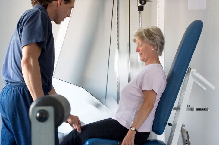 Eine Patientin macht Beinuebungen am Geraet unter Anleitung eines Physiotherapeuten in der Physiotherapie Praxis im VAMED Rehazentrum Karlsruhe