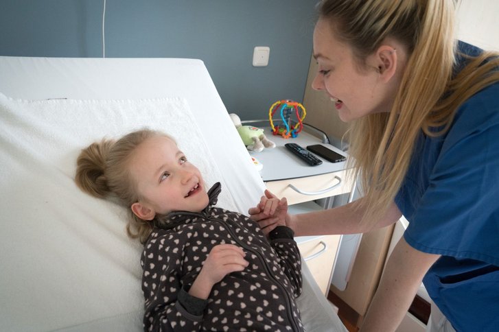 Maedchen liegt im Bett und lacht mit Pflegekraft