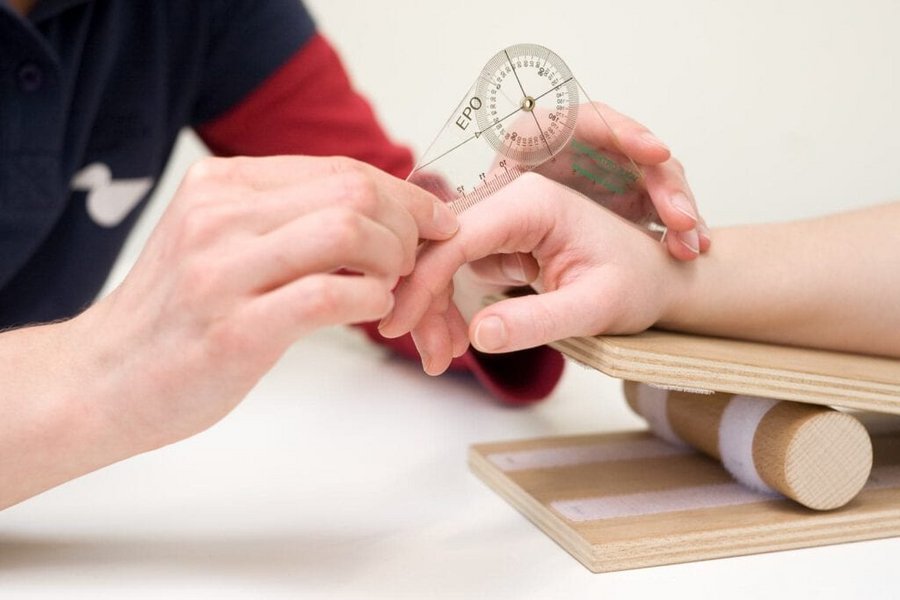 Nahaufnahme von Ergotherapeutenhaenden die die Fingergelenke eines Patienten ausmessen
