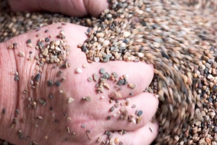 Nahaufnahme von zwei Haenden eines Patienten der wahrnehmungsfoerdernde Uebungen im Kies macht