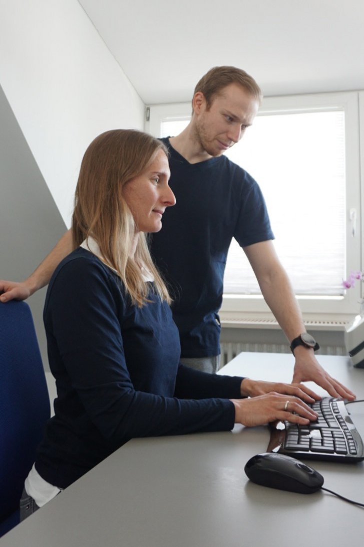 Therapeut berät eine Frau zur richtigen Einstellung des Bildschirmarbeitsplatzes