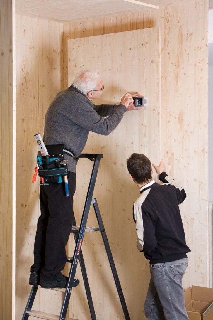Ein Patient schraubt im Stand auf einer Leiter etwas in die Wand, ein Therapeut begleitet dies