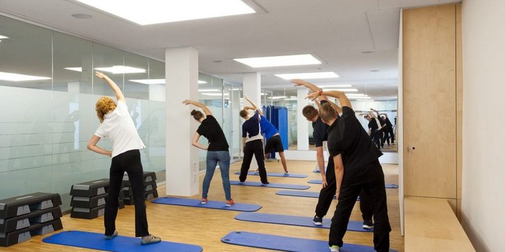 Blick von hinten auf eine Gruppe von sich im Stand nach links dehnenden Menschen