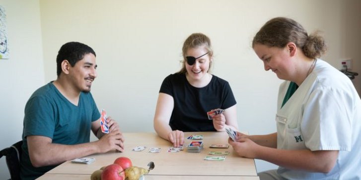 Junge Erwachsene und Erzieherin spielen Karten