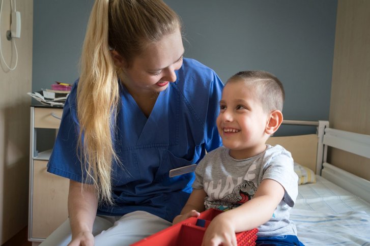 Junge und Pflegekraft sitzen auf einem Bett