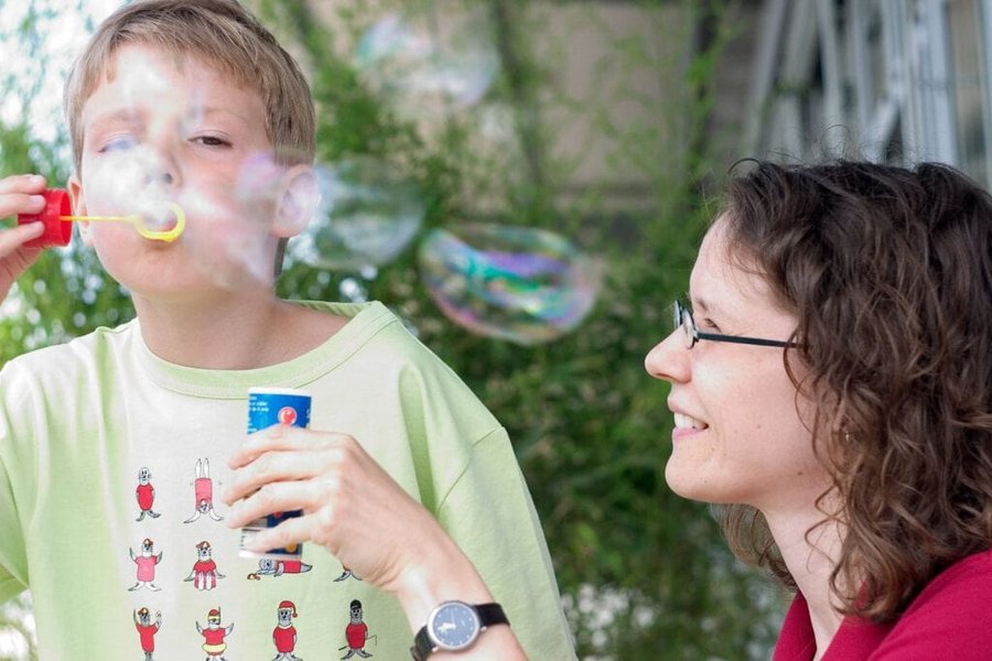 Ein Junge pustet Seifenblasen im Beisein einer Logopaedin bei der Therapie im Praxisbetrieb des VAMED Rehazentrum Karlsruhe