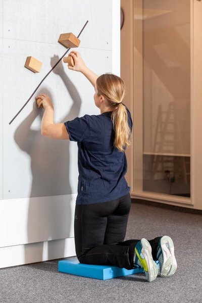 Eine Patientin arbeitet im Kniestand vor einer Wand im Rahmen der medizinisch beruflich orientierten Rehabilitation des VAMED Rehazentrums Karlsruhe