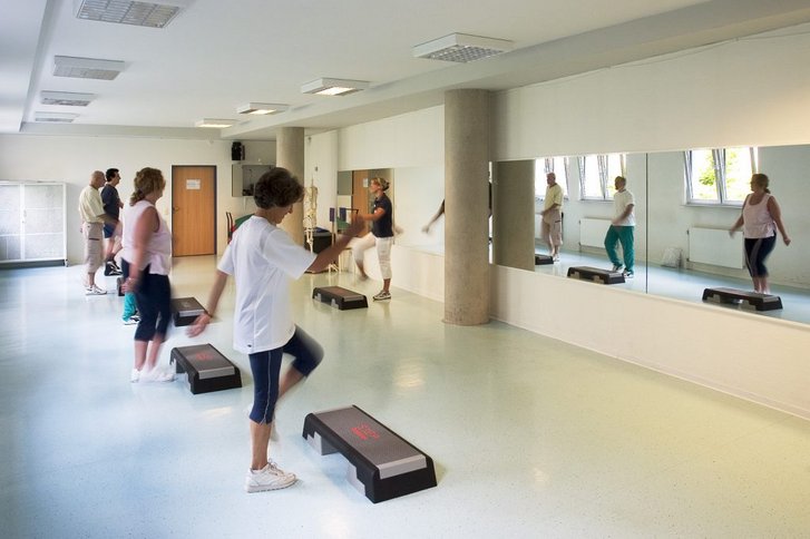 Patienten traineren in grossem Raum mit einem Stepper vor einer verspiegelten Wand