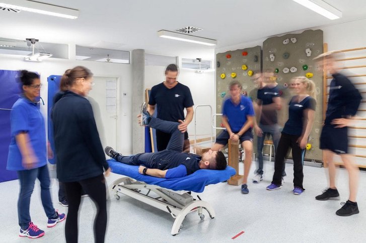 Eine Gruppe Physiotherapeuten steht im Rahmen einer Fortbildung um eine Liege an der Therapiemethoden vorgeführt werden