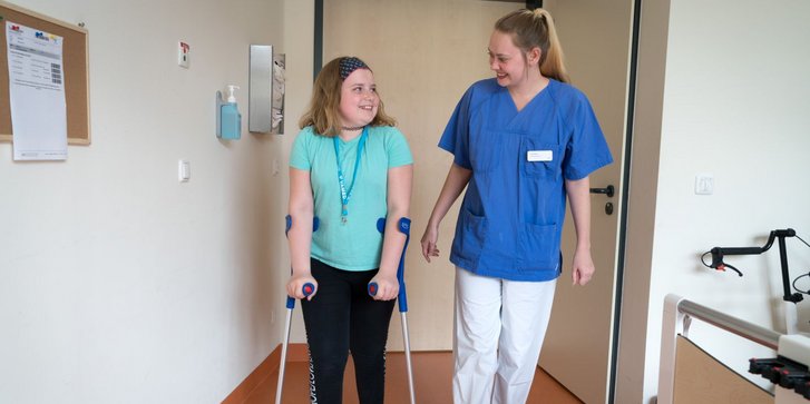 Maedchen uebt mit Pflegekraft Laufen