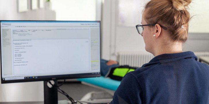 Eine Physiotherapeutin sitzt am PC und erstellt einen individuellen Behandlungsplan für einen Patienten in der Physiotherapie Abteilung des VAMED Rehazentrum Karlsruhe